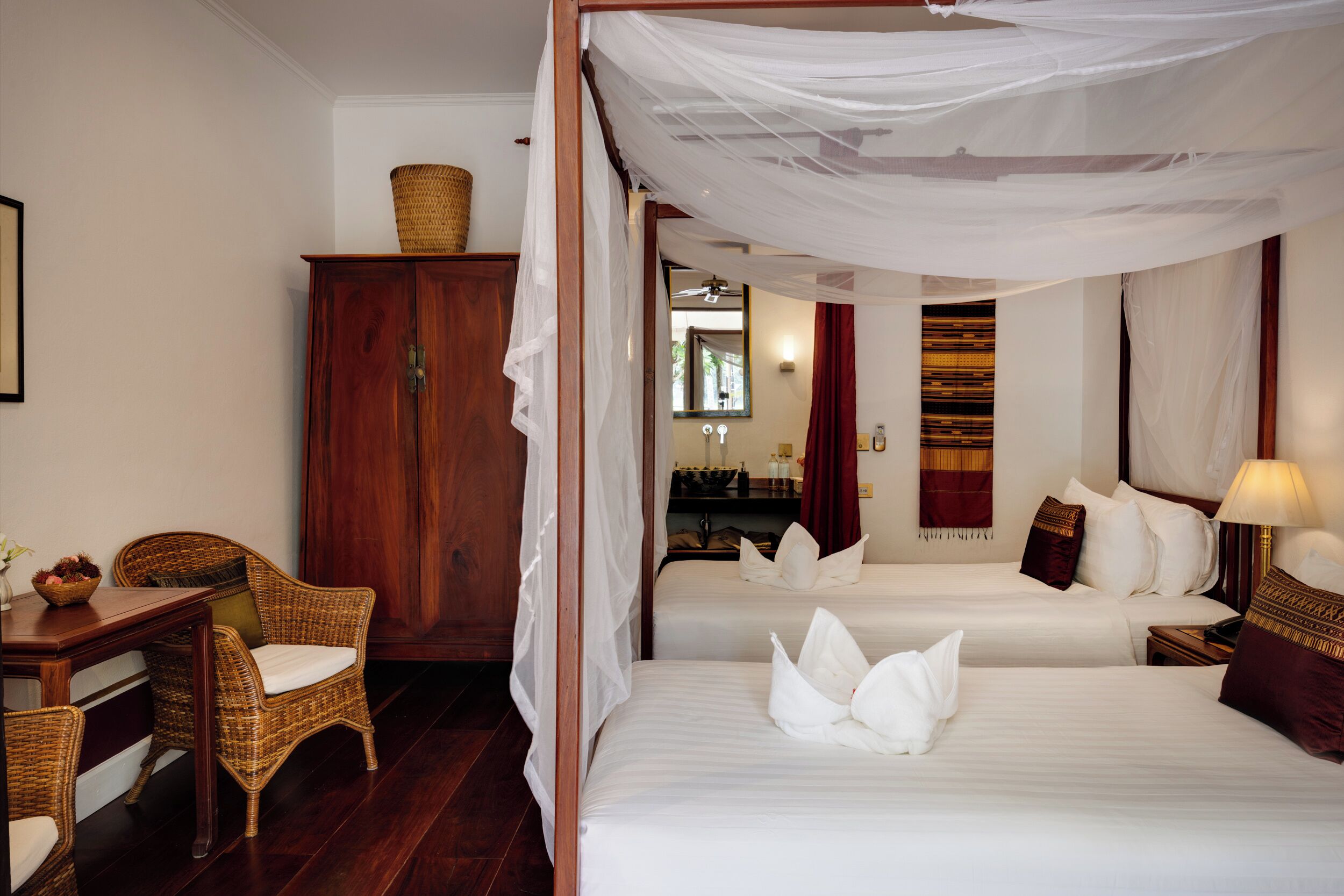 Una habitación de hotel con cama con dosel, un escritorio, una silla y un armario.