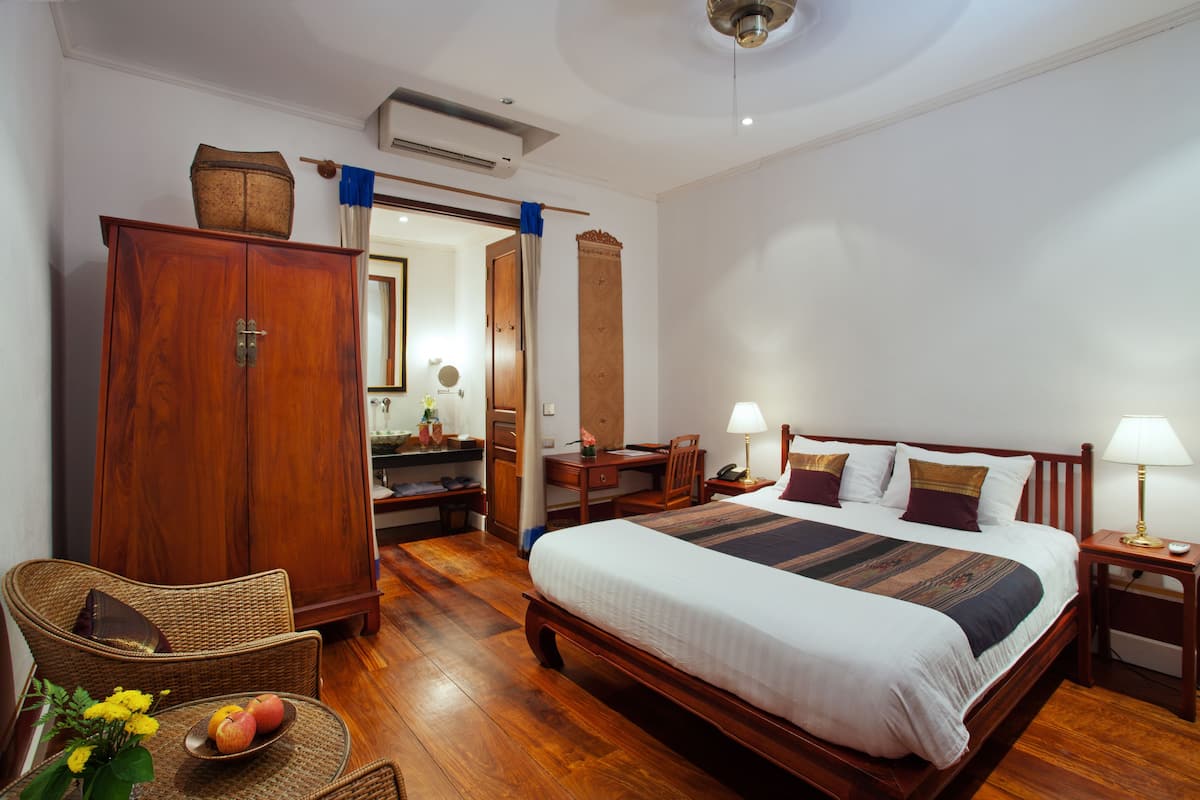 A hotel room with a large bed, wooden furniture, a desk, and a wardrobe.
