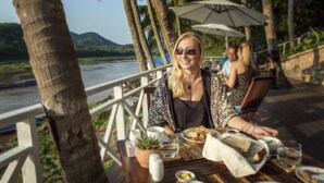 A dining table with food and drinks, a potted plant, and a view of a river and mountains. - The Belle Rive Boutique Hotel (Luang Prabang)