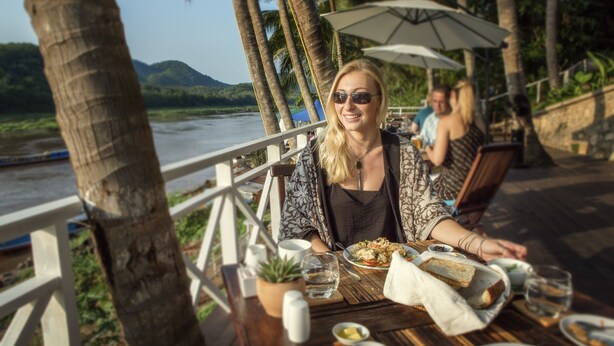 A dining table with food and drinks, a potted plant, and a view of a river and mountains. - The Belle Rive Boutique Hotel (Luang Prabang)