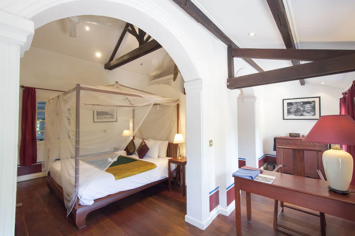 A bedroom with a four-poster bed, a desk with a lamp, and a framed picture on the wall.