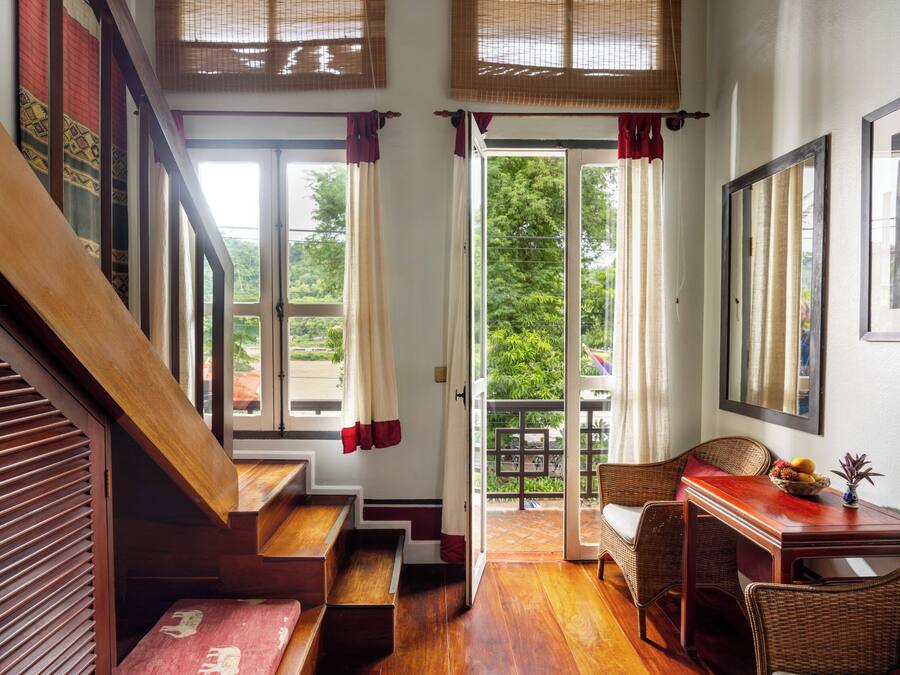 A staircase leading to a balcony with wicker furniture and a view of greenery outside.
