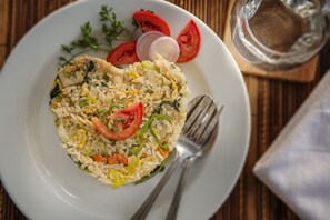 A plate of fried rice with vegetables and a glass of water on a wooden table.