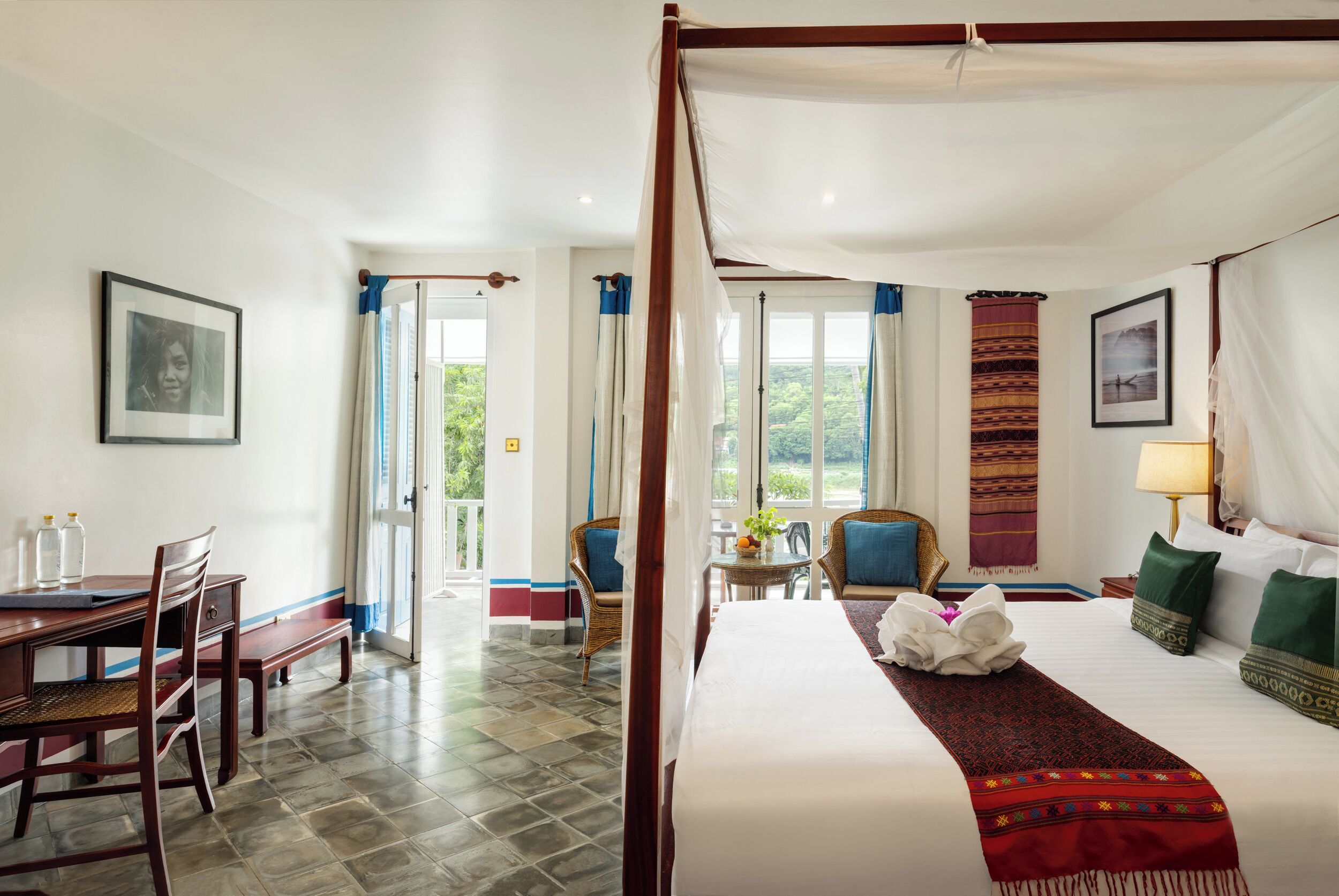 Habitación de hotel con cama con dosel, zona de comedor con mesa y sillas, y vistas al exterior.