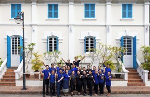 A group of people posing in front of a building with white walls and blue shutters. - The Belle Rive Boutique Hotel (Luang Prabang)