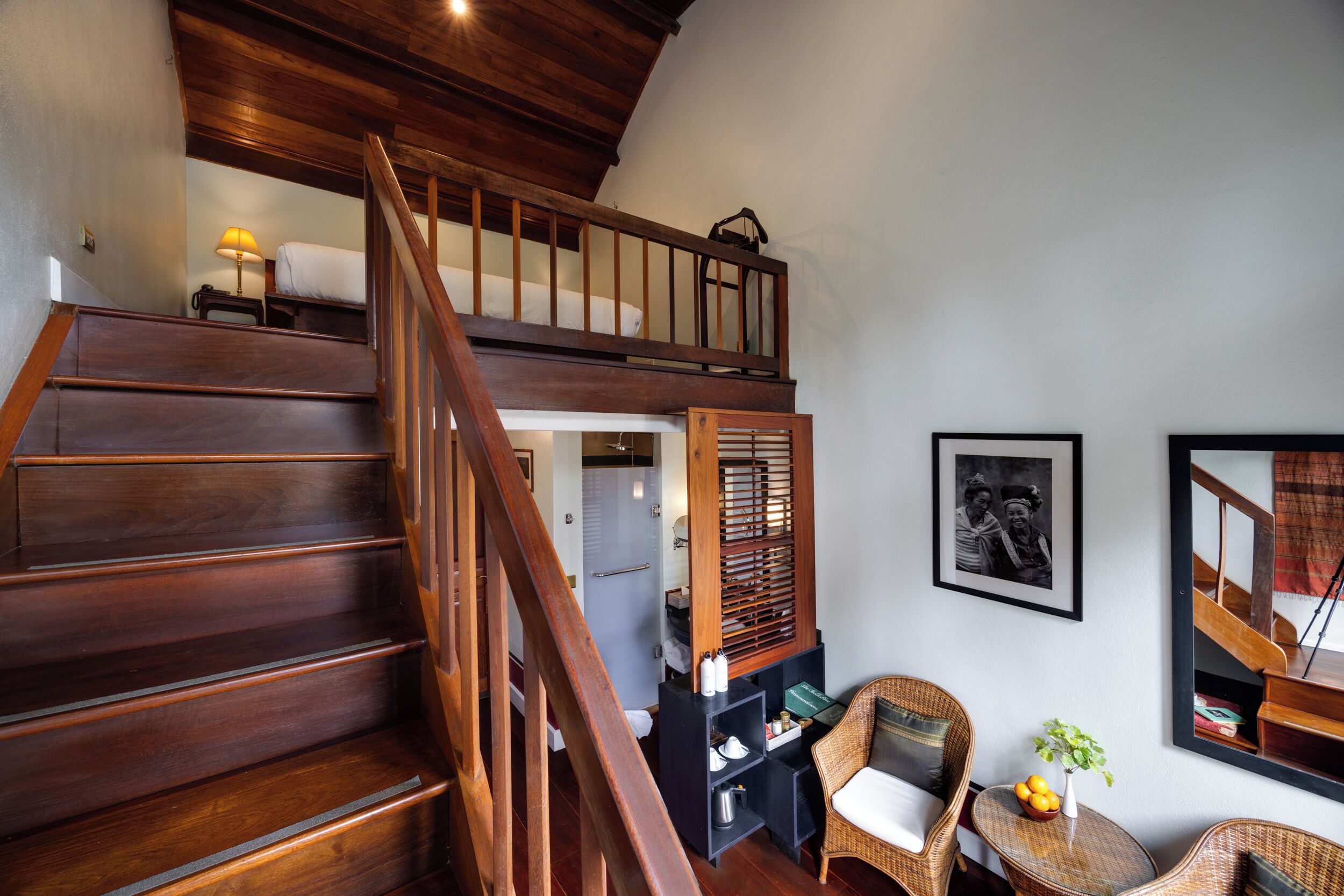 Una escalera de madera que conduce a un dormitorio en entrepiso con una cama y una mesita de noche.