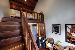 Una escalera de madera que conduce a un dormitorio en entrepiso con una cama y una mesita de noche.