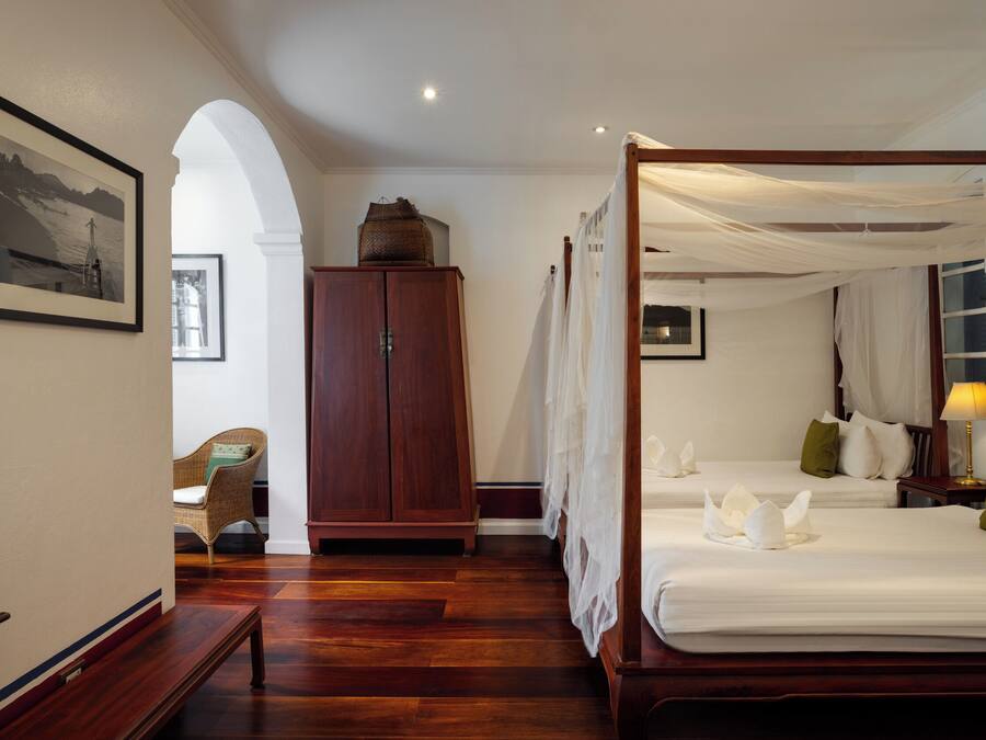 A four-poster bed with white linens and a canopy, a wooden wardrobe, and a framed picture on the wall.