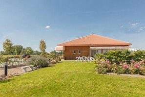 A modern house with a wooden exterior and a red roof, surrounded by a well-maintained lawn and garden. - Pressoir Hôtel (Saint-Calais)