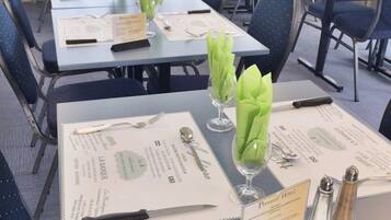 Comedor de hotel con mesas preparadas para el servicio, menús y porta servilletas verdes.