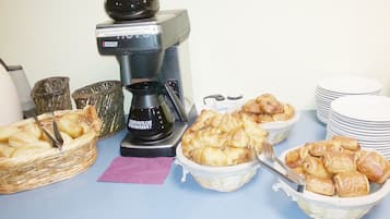 Una mesa de buffet con diferentes tipos de comida, una cafetera y platos apilados.