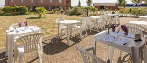 Un patio al aire libre con mesas y sillas de plástico blanco, un edificio al fondo y suelo de grava.