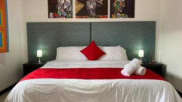A hotel room with a large bed, red and white bedding, two nightstands with lamps, and three paintings on the wall.