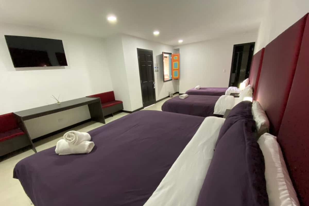 A hotel room with two beds, a flat-screen TV, a desk, and a red couch.