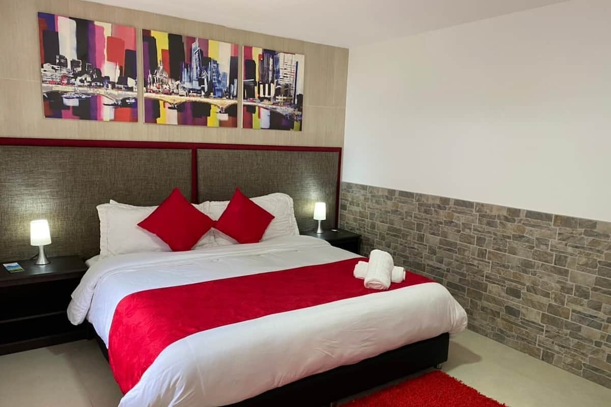A modern hotel room with a large bed, red and white bedding, a red throw blanket, and a cityscape artwork above the bed.