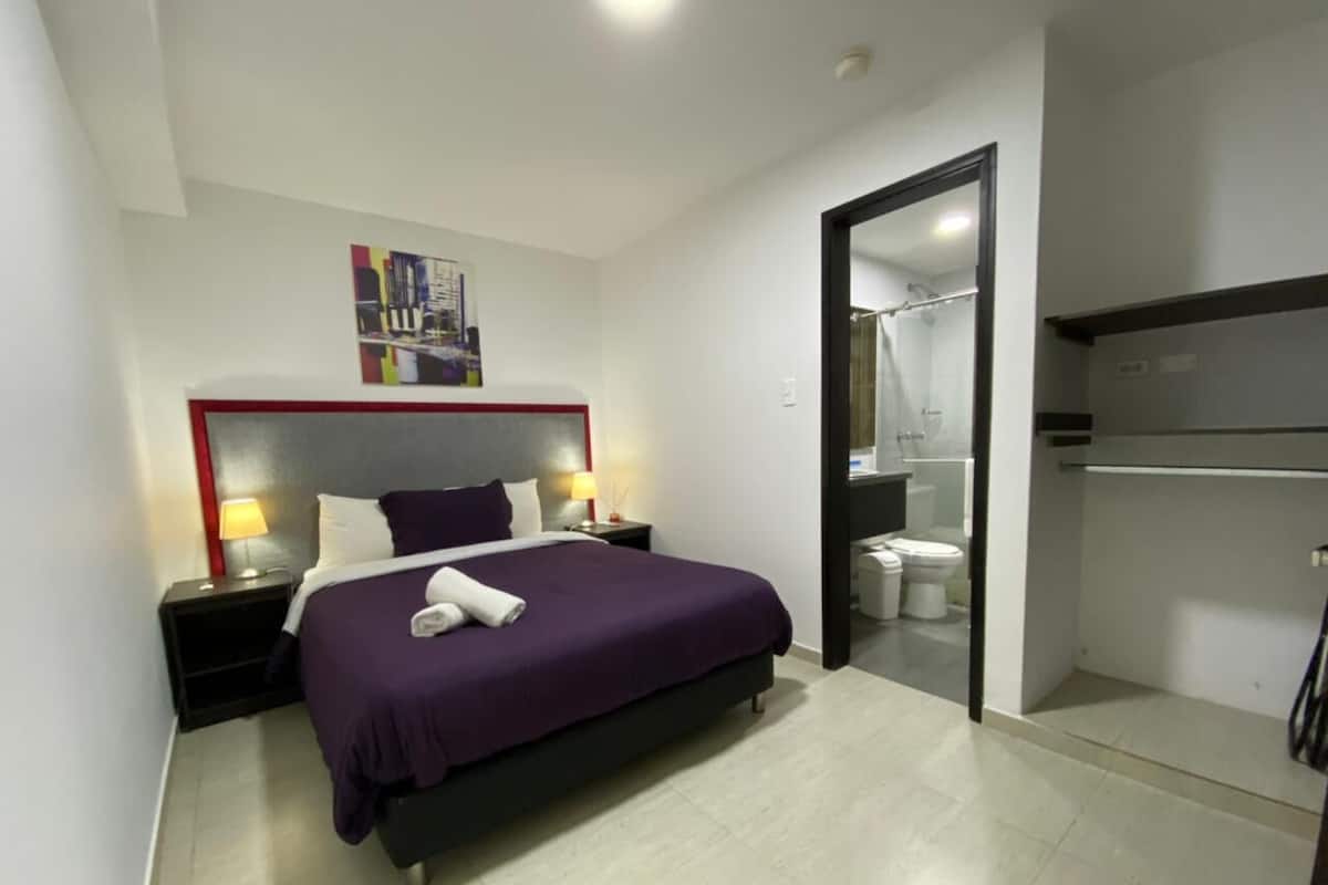 A modern hotel room with a large bed, bedside tables, a bathroom, and a wardrobe.