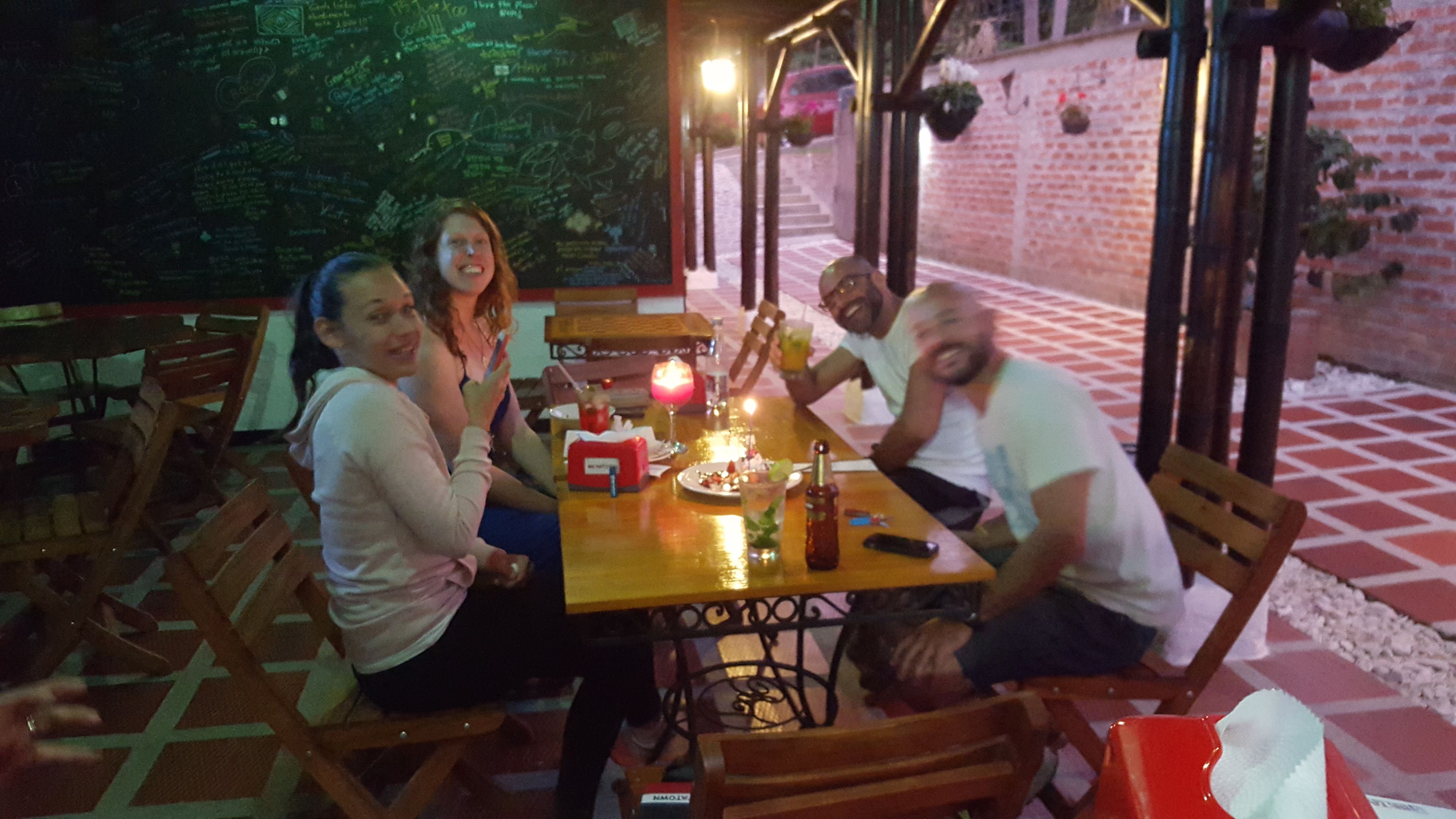 A group of people seated around a wooden table with a candle, drinks, and a menu.