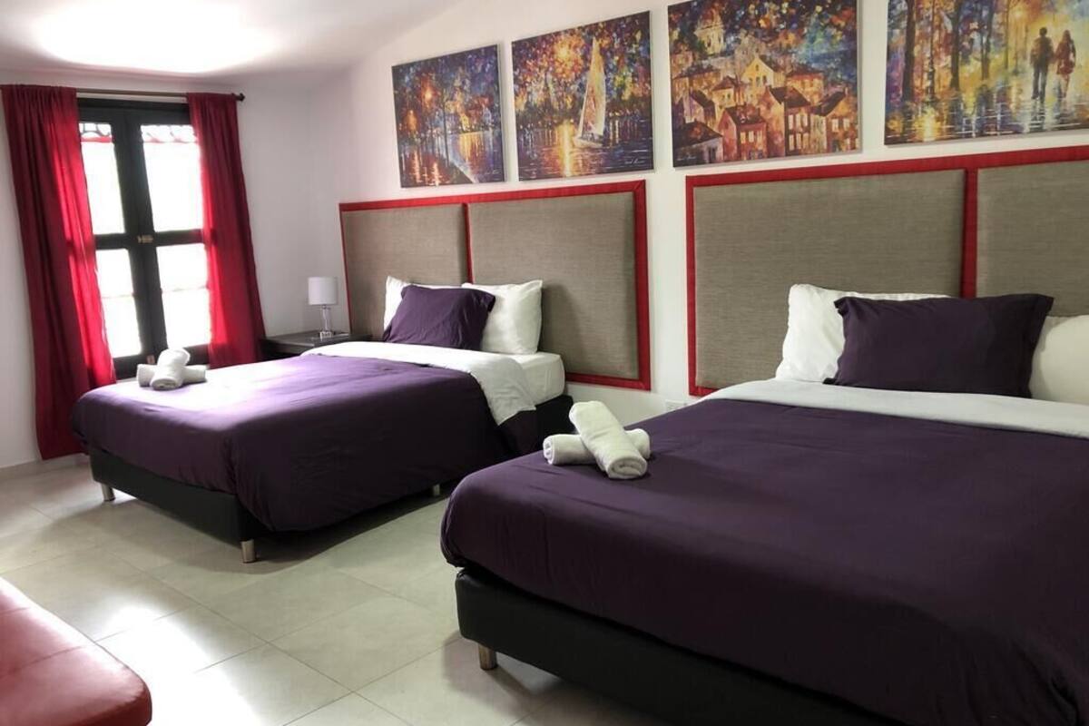 A hotel room with two beds, red curtains, and artwork on the wall.