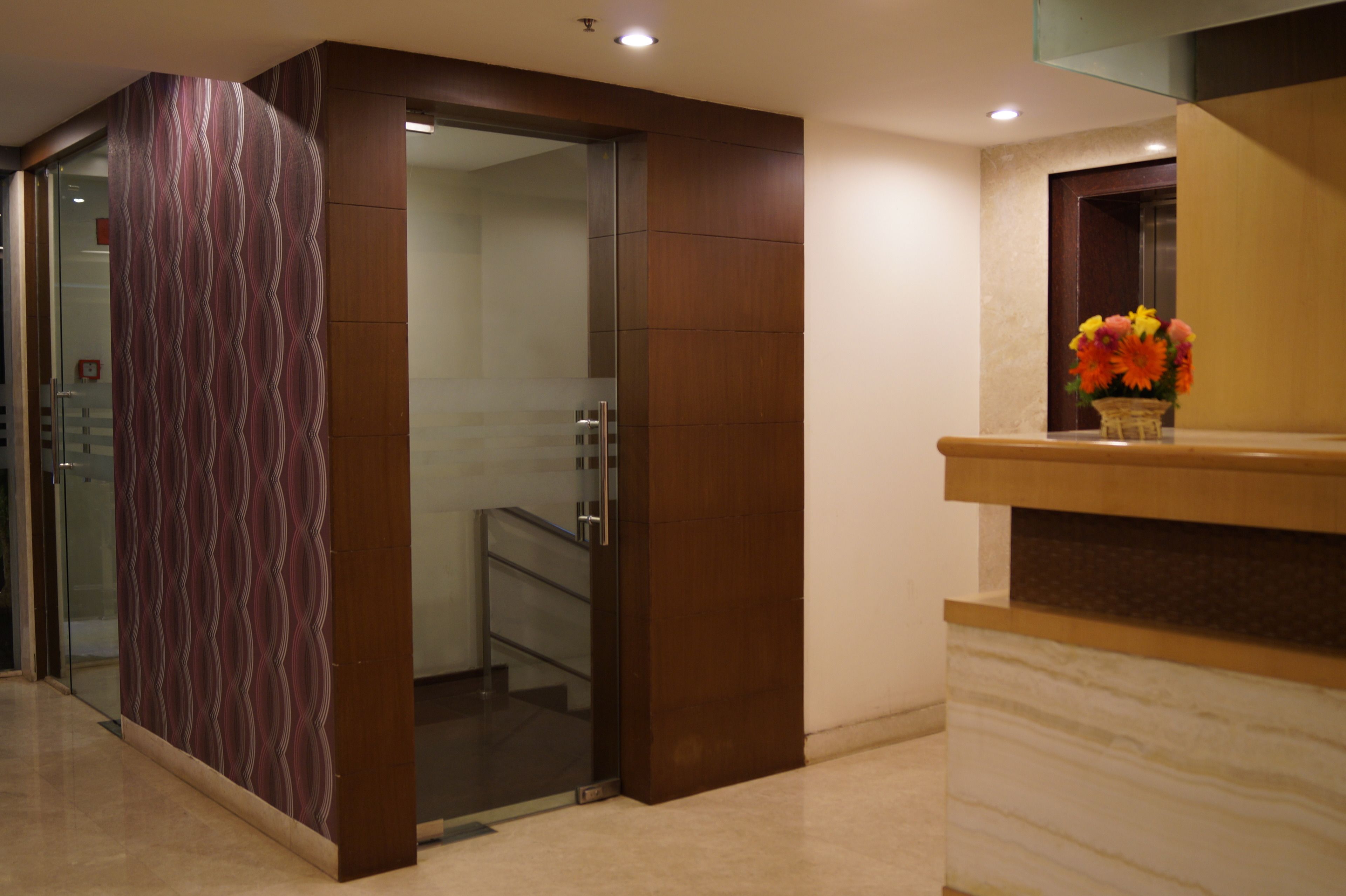 A modern reception area with a marble counter, a glass door leading to a staircase, and a decorative panel with a wavy pattern.