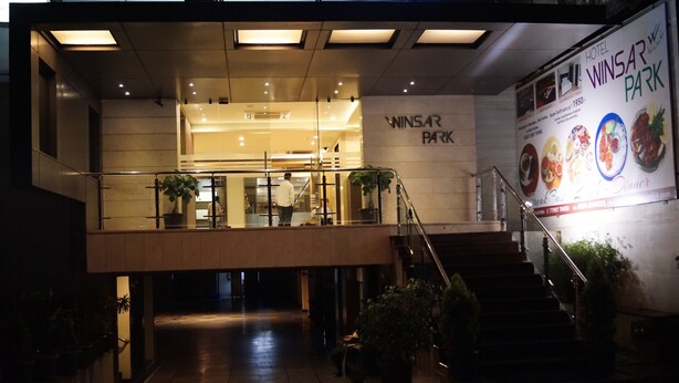 Ein Hotel Eingang mit einer Treppe, die zu einer oberen Ebene führt, einem Schild für Winsar Park und einem Banner, das die Restaurants des Hotels bewirbt.