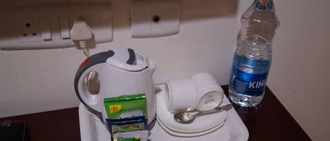 A tray with a kettle, a cup, a spoon, a water bottle, and a pack of tissues.