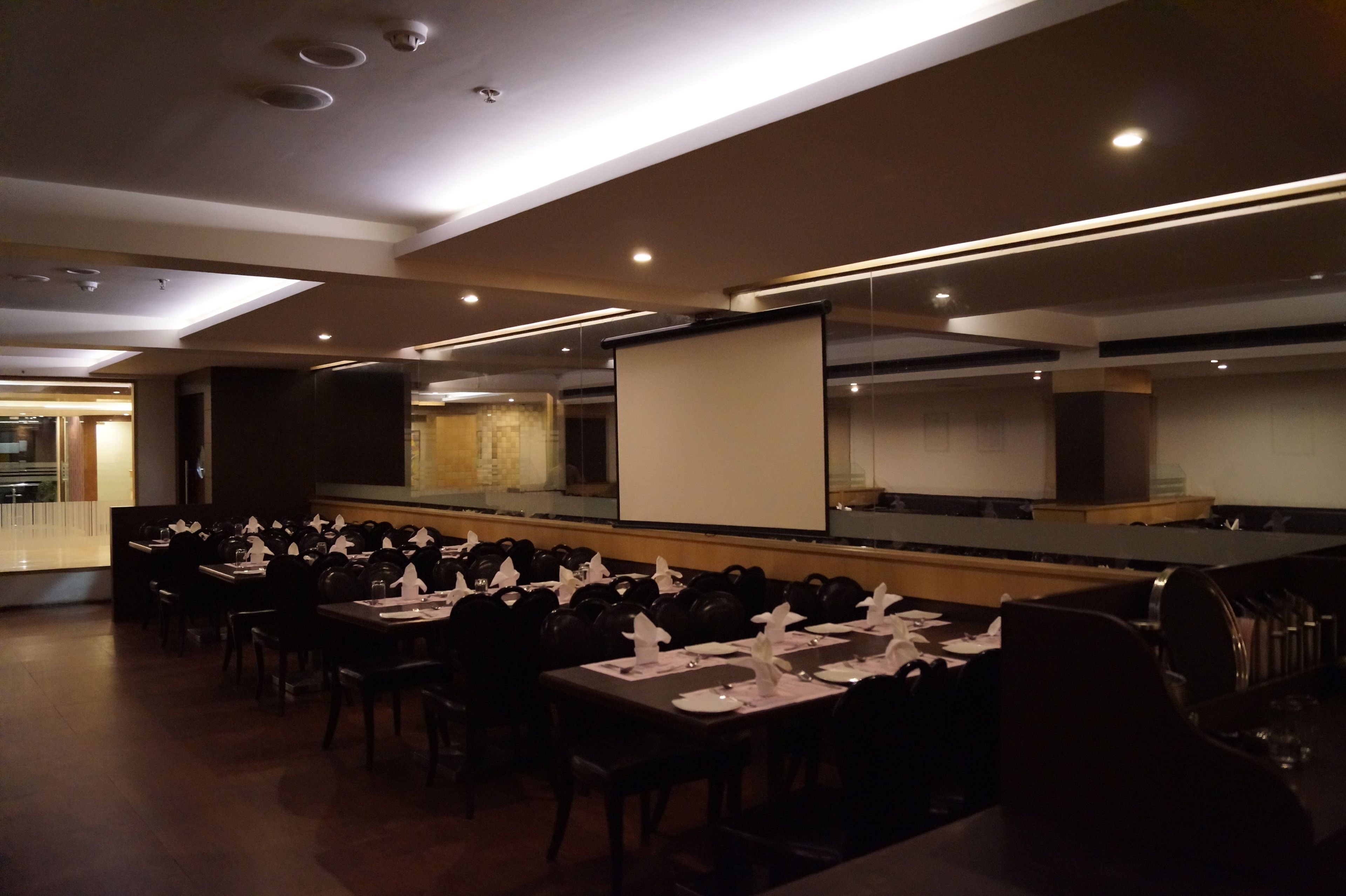 A conference room with multiple tables and chairs, a large screen, and a stage.