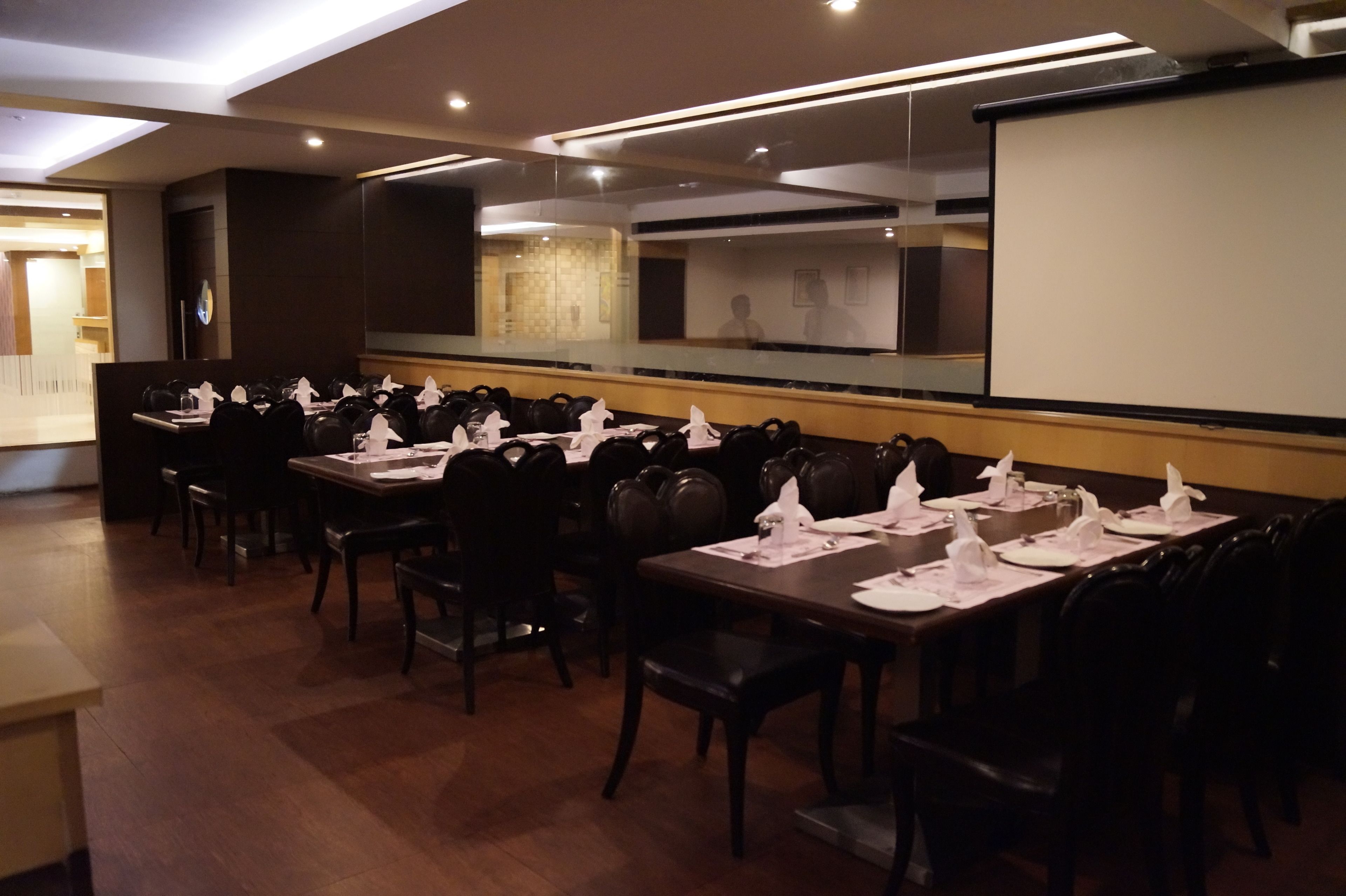 A conference room with multiple tables set for a meeting, equipped with chairs and a large projection screen.