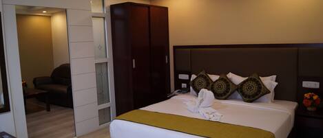 A hotel room with a large bed, a wardrobe, a seating area with a chair, and a small table.