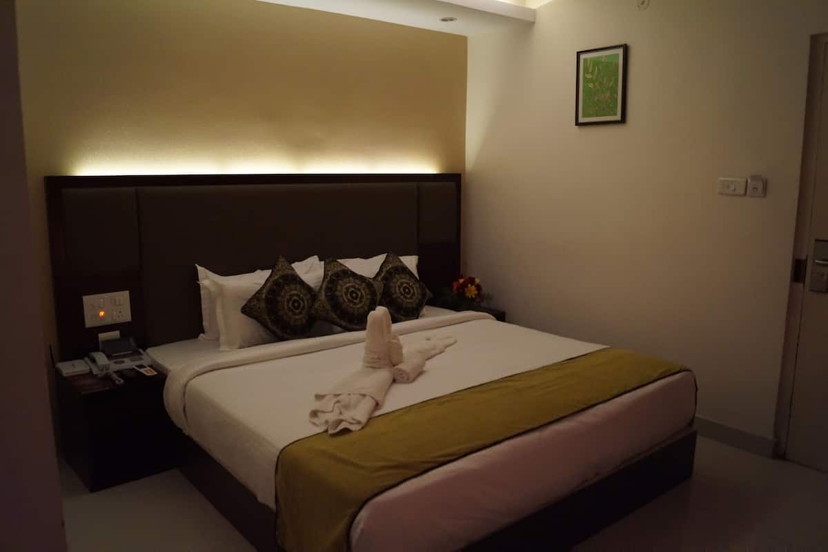 A hotel room with a large bed, a nightstand with a phone, and a wall-mounted light.