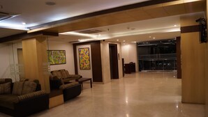 Eine großzügige Lobby mit modernem Design, ausgestattet mit einer Sitzecke mit Sofas und einer Bank, einem großen abstrakten Gemälde an der Wand und einem Glasgang zu einem weiteren Bereich.