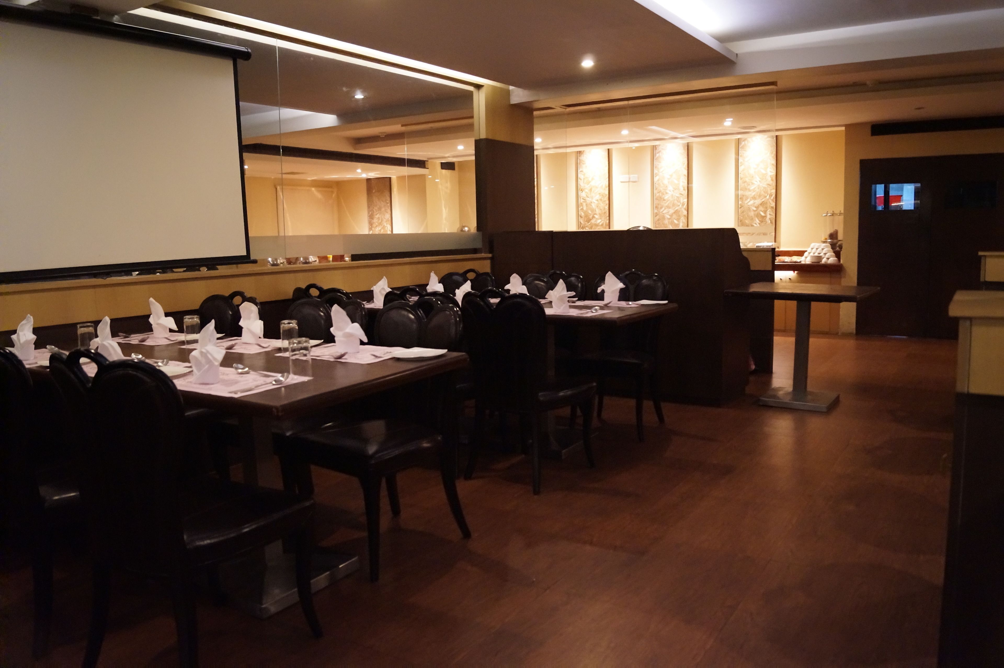 Una sala de conferencias con una pantalla grande, varias mesas con sillas y una zona de recepción al fondo.
