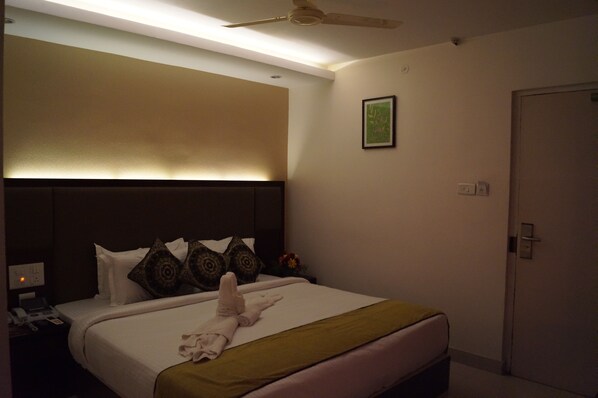 Una habitación de hotel con cama, mesita de noche, teléfono, ventilador de techo y puerta.