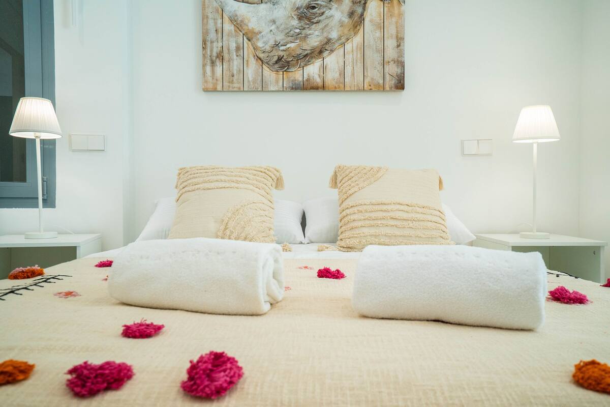 A neatly made bed with towels, a painting on the wall, and two bedside lamps.