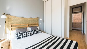 A neatly made bed with a striped blanket, a woven headboard, and two bedside lamps. - SmartRental Madrid Puerta del Sol (Madrid)