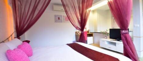 A bedroom with a bed, a TV, a desk, and a mirror.