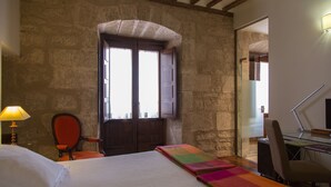 Ein Zimmer mit einem Bett, einem Schreibtisch, einem Stuhl, einer Lampe und einem Fenster mit Holzläden.