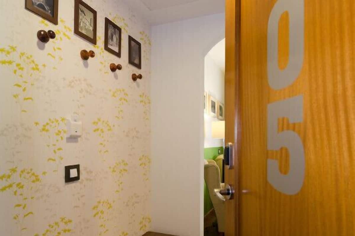 Un pasillo con un papel tapiz decorativo, una puerta de madera con un número y un banco.