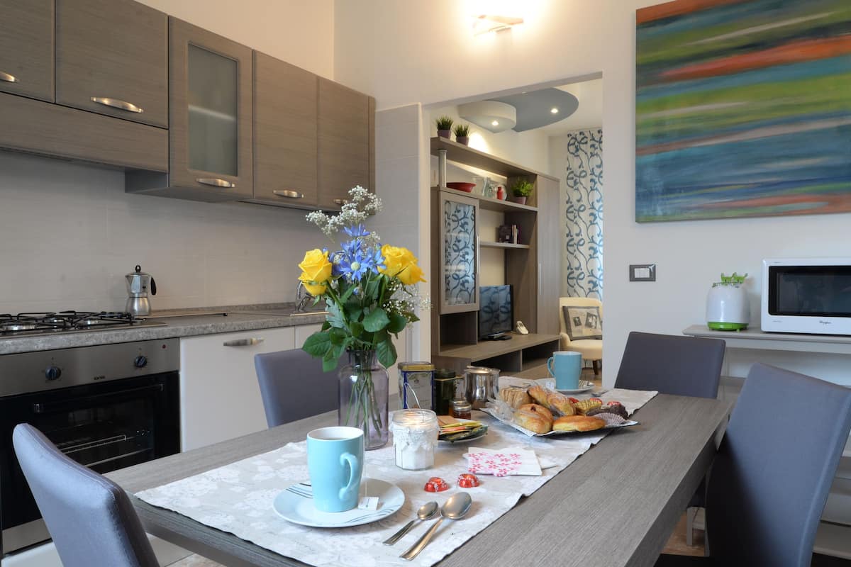A modern kitchen with grey cabinets, a dining table set with a blue cup, a vase with yellow flowers, and a tray of pastries.