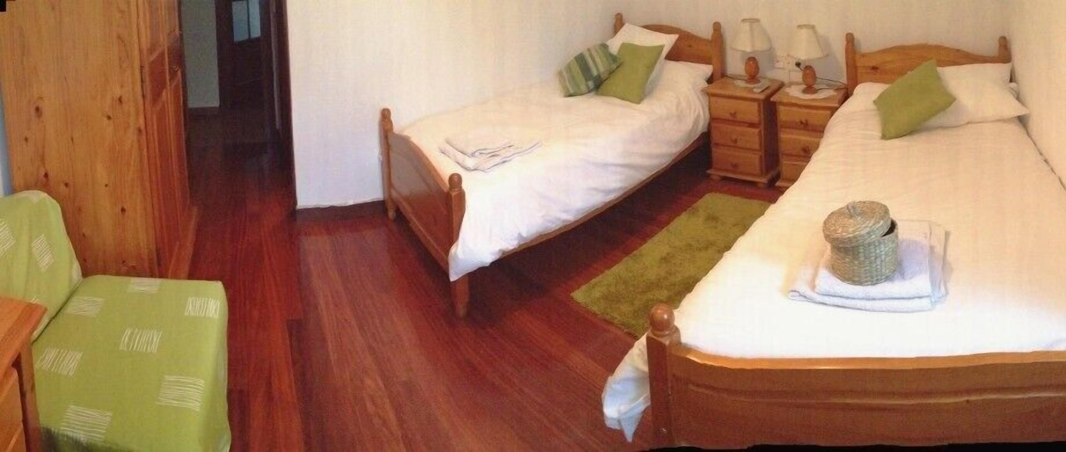Una habitación con dos camas individuales, mesitas de noche de madera y una silla verde.
