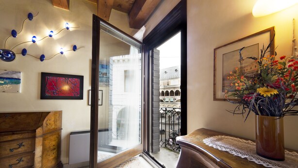 Una stanza con un comò in legno, una porta vetrata che dà su un balcone e un vaso con fiori su un tavolo.