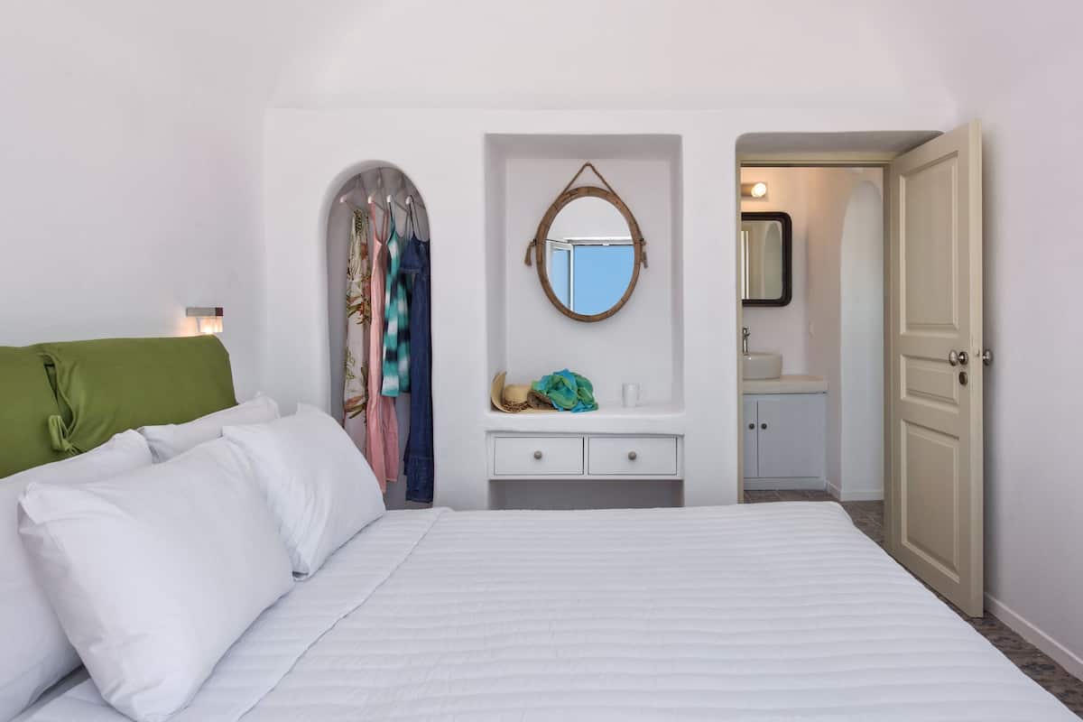 A neatly arranged bedroom with a bed, a vanity with a mirror, and a door leading to a bathroom.