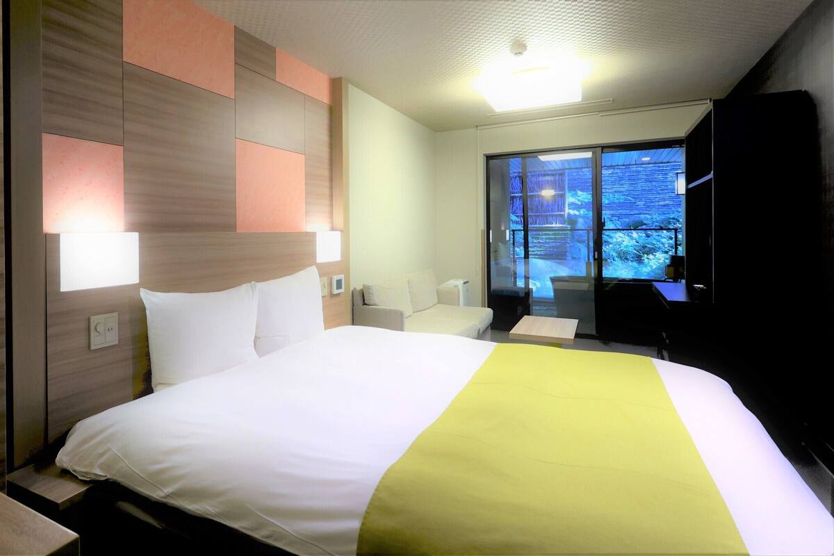 A hotel room with a bed, bedside tables, a desk, a chair, a TV, and a window with a view.