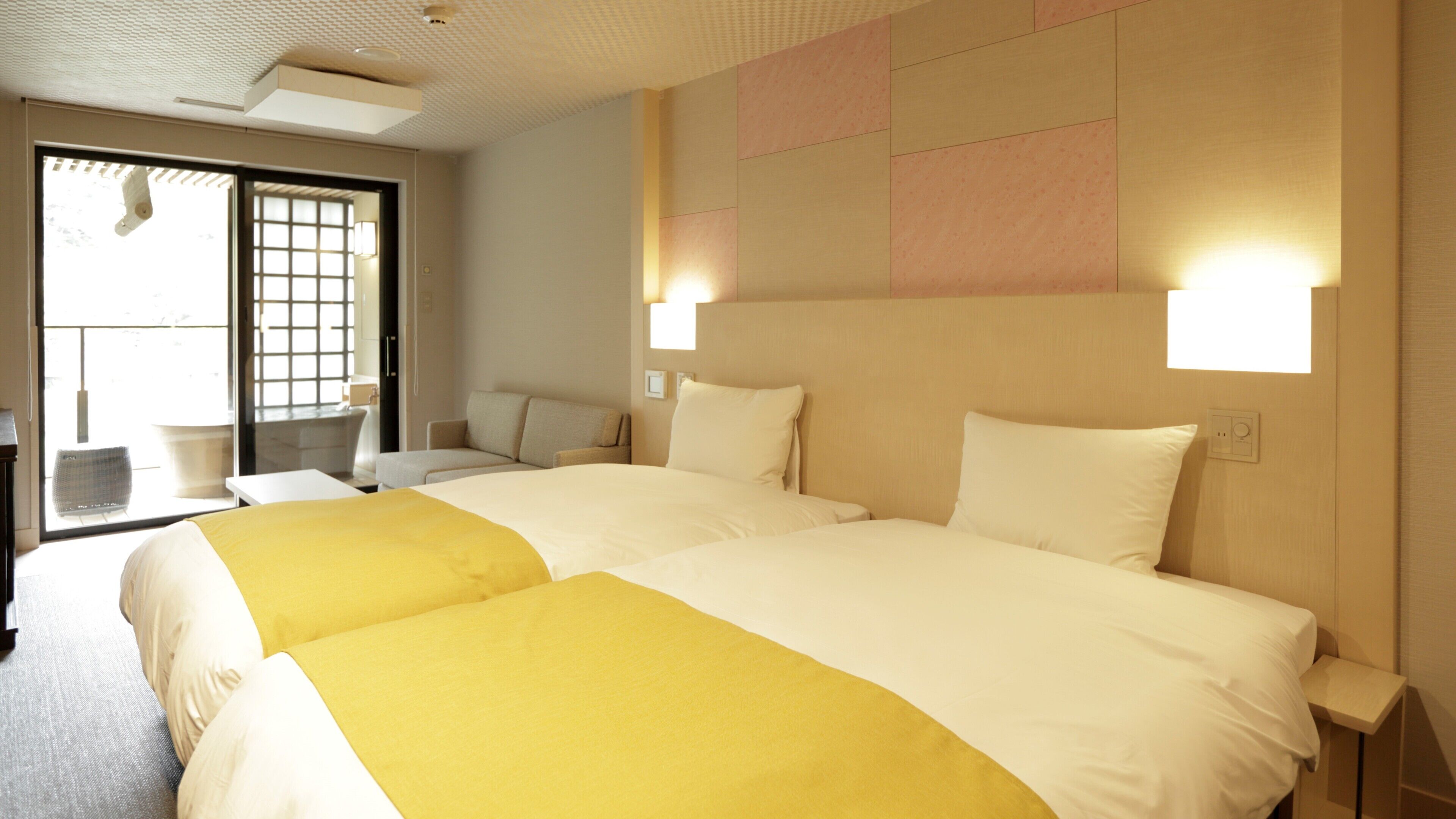 Ein Hotelzimmer mit zwei Betten, einem Schlafsofa, einem kleinen Tisch und Blick durch ein Fenster.