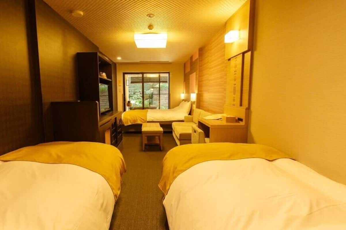 A hotel room with two beds, a desk, a chair, a TV, and a window.