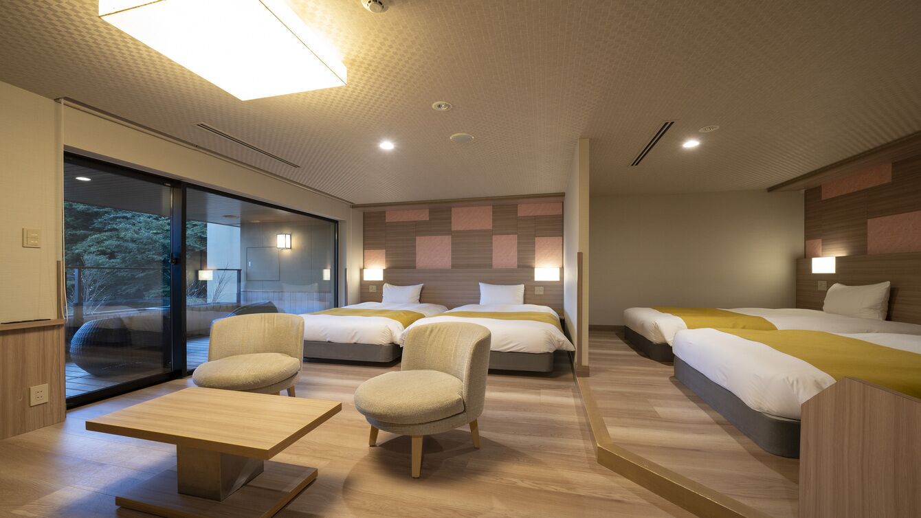 Ein modernes Hotelzimmer mit einer großen Schiebeglasdoor, zwei Betten mit gelber Bettwäsche, einer kleinen Couch und einem Holztisch.