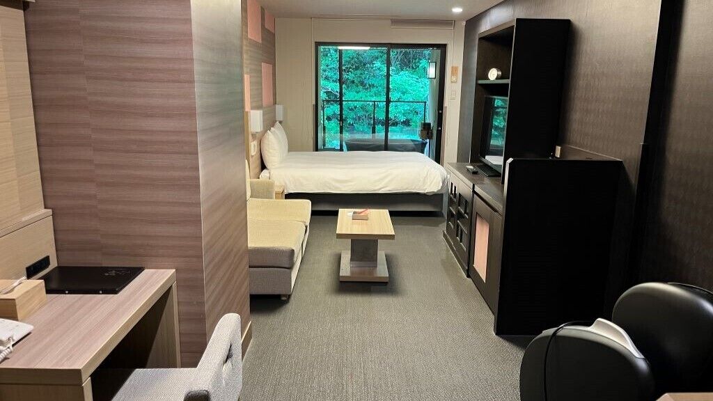 Ein Hotelzimmer mit Bett, Schreibtisch, Stuhl, Fernseher und Blick ins Grüne.
