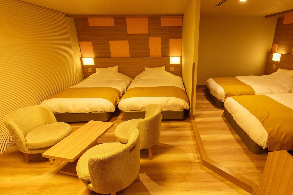 A hotel room with four single beds, a sofa, and a small table.