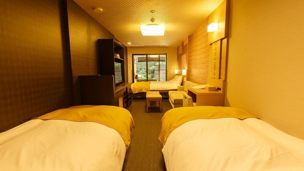 Ein Hotelzimmer mit zwei Betten, einem Schreibtisch, einem Sessel, einem Fernseher und einem Fenster.
