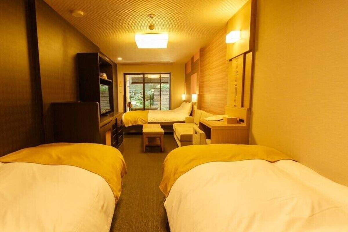 A hotel room with two beds, a desk, a chair, a television, and a window.