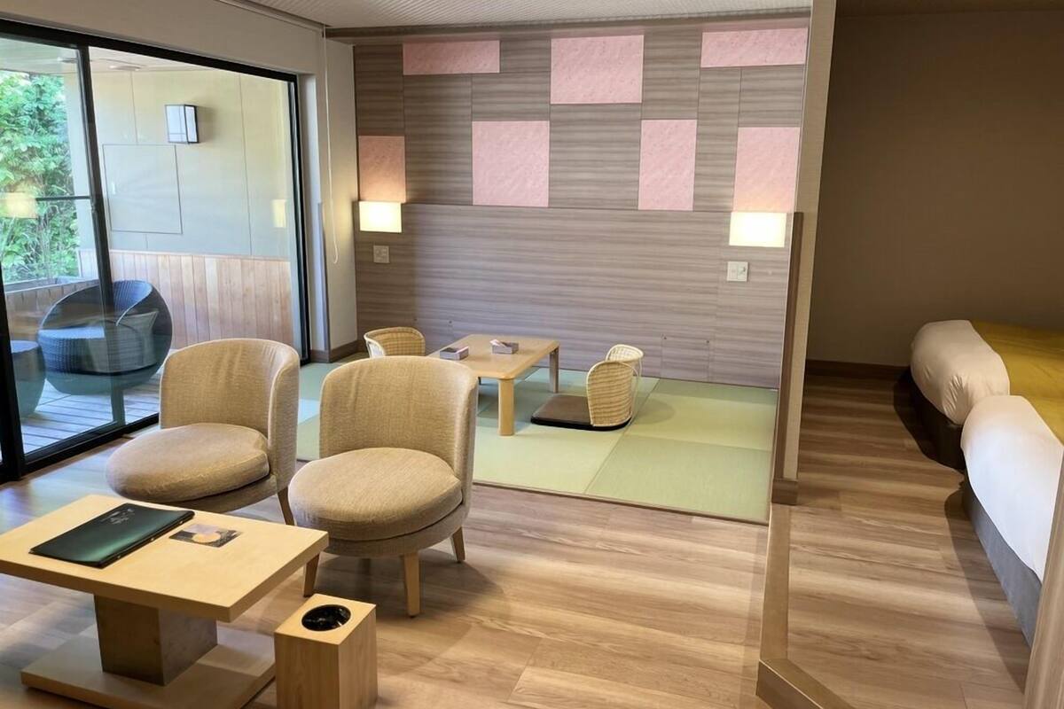 A modern hotel room with a wooden floor, a sofa, a dining table, and chairs.